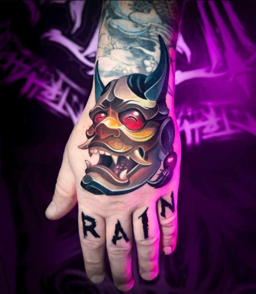 Тату на кисти, нео-трад: маска Хання и надпись на пальцах. Работа студии Ink Masters.